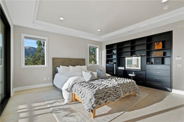 bedroom with light hardwood / wood-style floors, a raised ceiling, and multiple windows