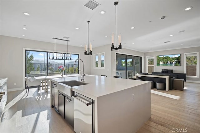 kitchen with light wood-type flooring, decorative light fixtures, plenty of natural light, and a kitchen island with sink