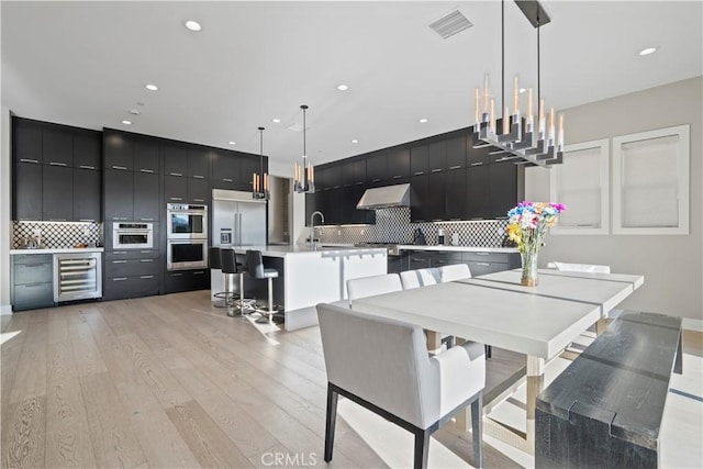 dining area with sink, beverage cooler, and light hardwood / wood-style flooring