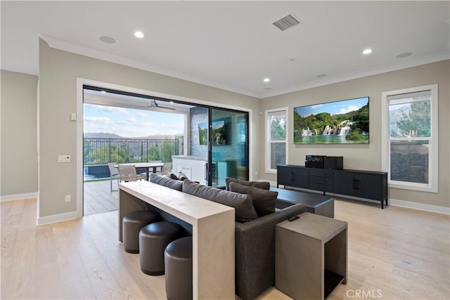 living room with light hardwood / wood-style floors, ornamental molding, ceiling fan, and a healthy amount of sunlight