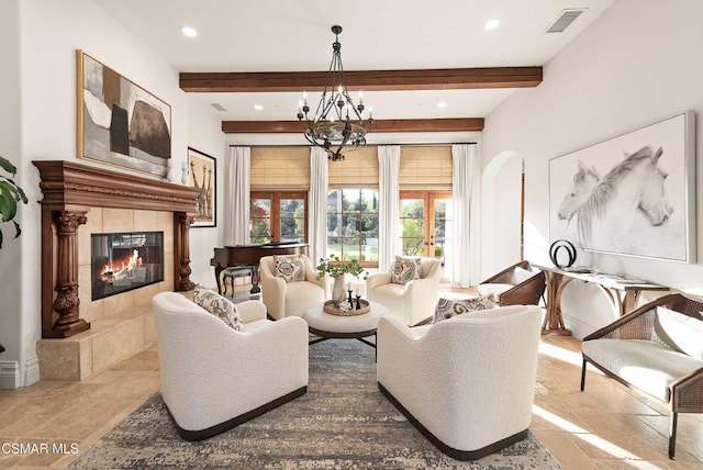 living room with a notable chandelier, a tiled fireplace, french doors, and beamed ceiling