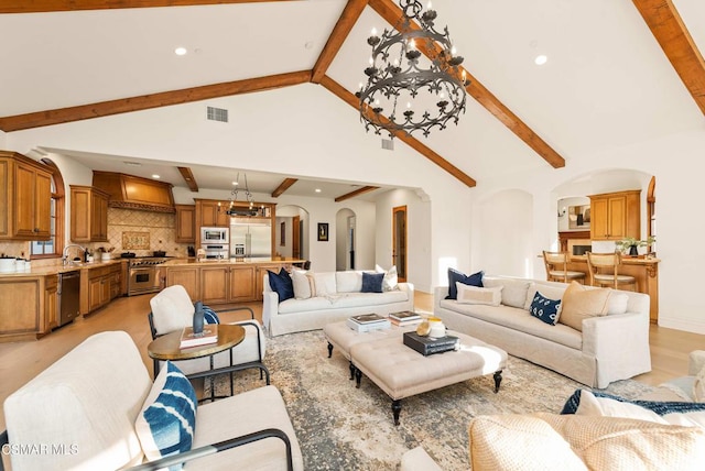 living room with a chandelier, beam ceiling, light hardwood / wood-style flooring, and high vaulted ceiling