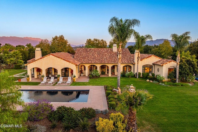 back house at dusk with a patio area, a yard, and a mountain view