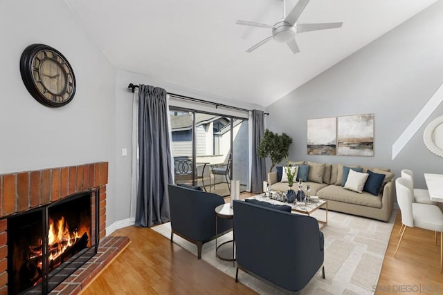 living room with wood-type flooring, lofted ceiling, ceiling fan, and a brick fireplace