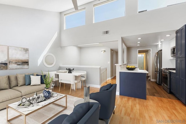 living room featuring a high ceiling, plenty of natural light, sink, and light hardwood / wood-style floors