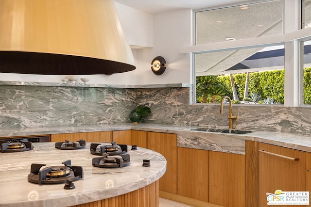 kitchen with exhaust hood, light stone countertops, decorative backsplash, and sink