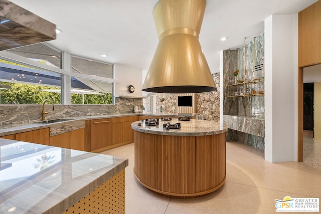 kitchen featuring stainless steel gas cooktop, decorative backsplash, light stone counters, and sink