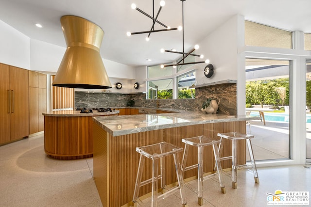 kitchen with an inviting chandelier, kitchen peninsula, backsplash, high vaulted ceiling, and a breakfast bar