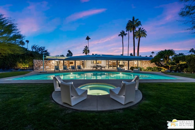 pool at dusk featuring an in ground hot tub, a lawn, and a patio