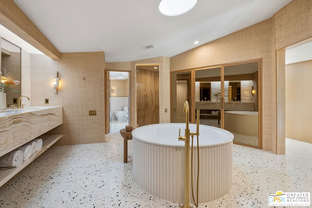 bathroom with a washtub, toilet, vanity, and lofted ceiling