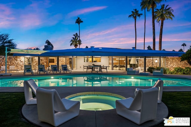 pool at dusk featuring a patio and an in ground hot tub