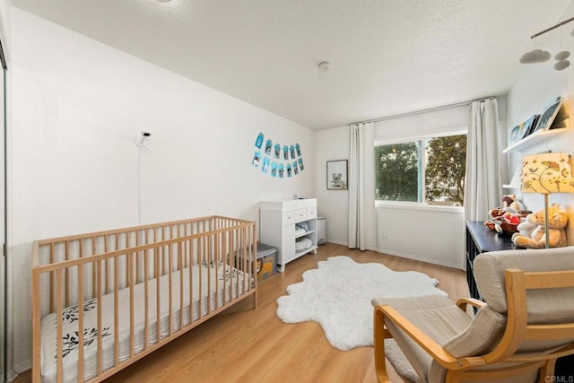 bedroom with a crib, a textured ceiling, and hardwood / wood-style flooring