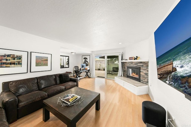 living room featuring wood-type flooring, a stone fireplace, and a textured ceiling