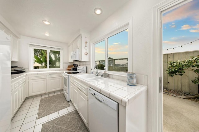 kitchen with white appliances, white cabinetry, sink, tile countertops, and light tile patterned floors