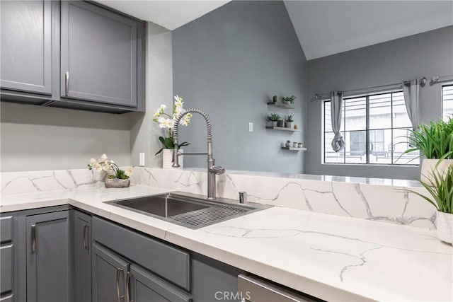 kitchen with light stone counters, sink, gray cabinets, and vaulted ceiling