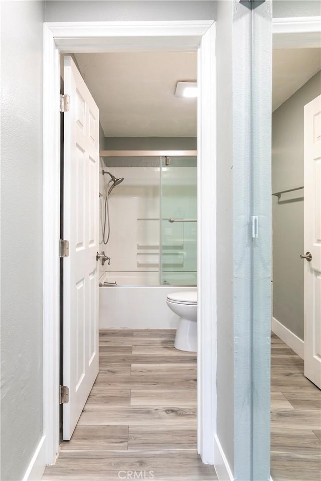 bathroom featuring bath / shower combo with glass door, hardwood / wood-style floors, and toilet