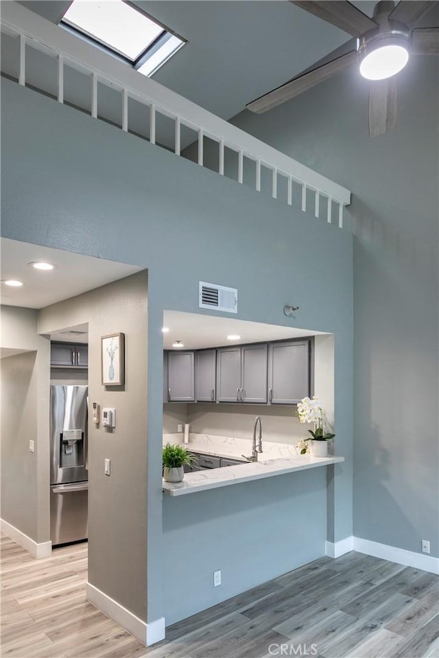 kitchen with sink, gray cabinetry, kitchen peninsula, stainless steel refrigerator with ice dispenser, and light hardwood / wood-style flooring