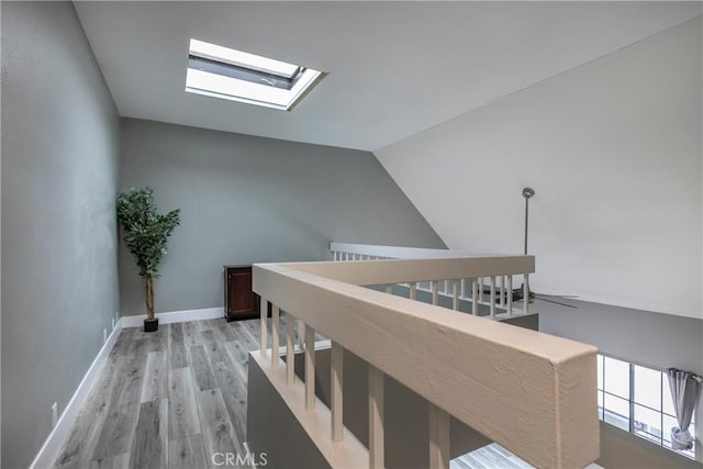 hall featuring vaulted ceiling with skylight and light wood-type flooring