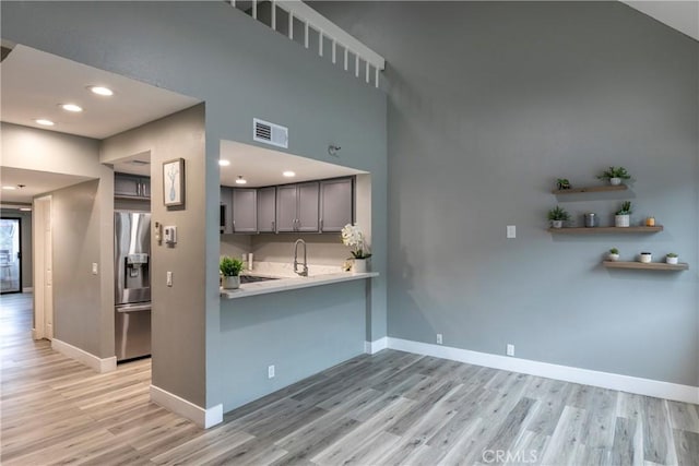 kitchen with sink, stainless steel fridge with ice dispenser, light hardwood / wood-style flooring, gray cabinets, and kitchen peninsula