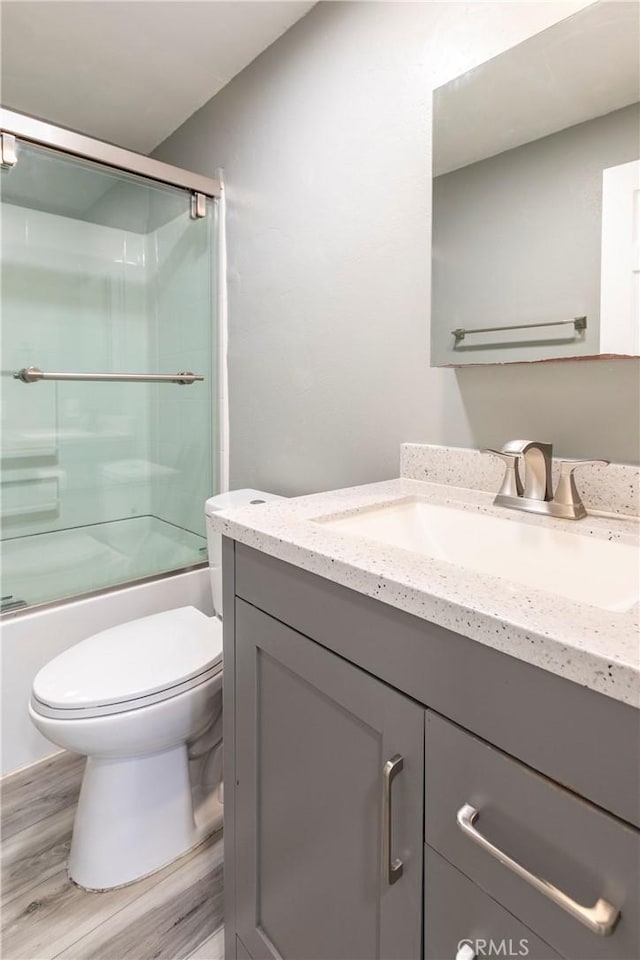 full bathroom with bath / shower combo with glass door, wood-type flooring, toilet, and vanity