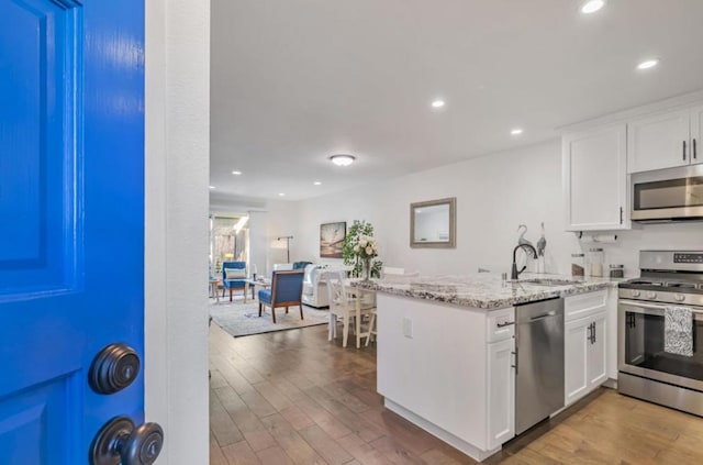 kitchen with sink, stainless steel appliances, light stone countertops, white cabinets, and kitchen peninsula