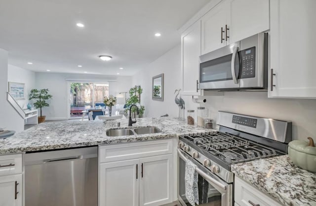 kitchen featuring sink, light stone counters, appliances with stainless steel finishes, kitchen peninsula, and white cabinets