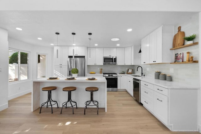 kitchen featuring decorative light fixtures, appliances with stainless steel finishes, white cabinetry, and a kitchen island