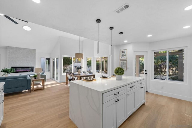 kitchen with light wood-type flooring, white cabinetry, a tile fireplace, and decorative light fixtures