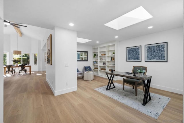 office area featuring ceiling fan, light hardwood / wood-style floors, built in shelves, and lofted ceiling with skylight