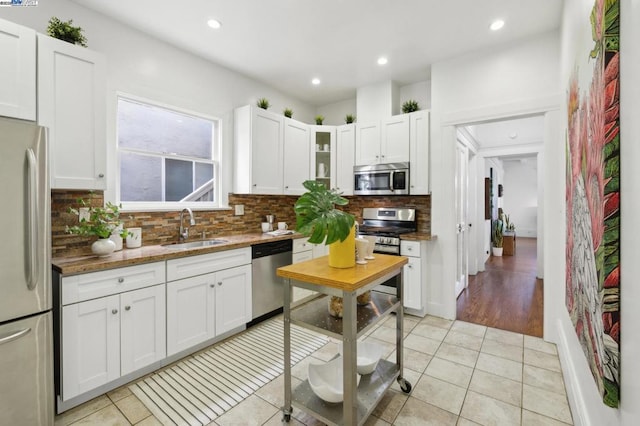 kitchen featuring light tile patterned flooring, sink, white cabinetry, appliances with stainless steel finishes, and backsplash