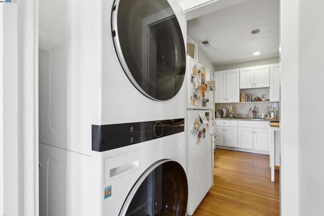 clothes washing area with stacked washer / dryer, sink, and light hardwood / wood-style flooring