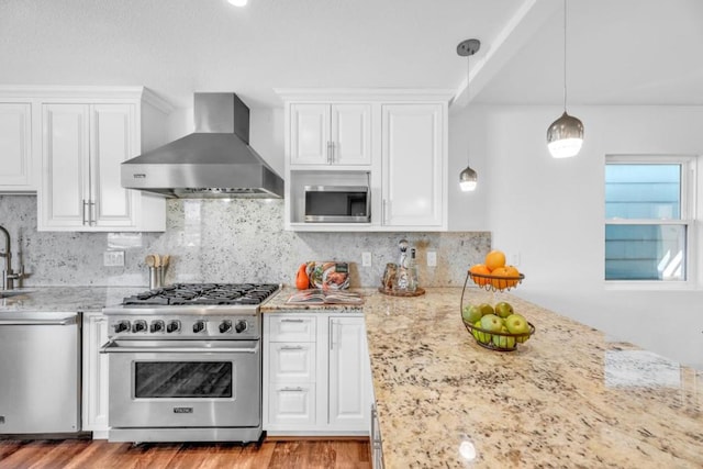 kitchen with appliances with stainless steel finishes, white cabinets, hanging light fixtures, and wall chimney exhaust hood