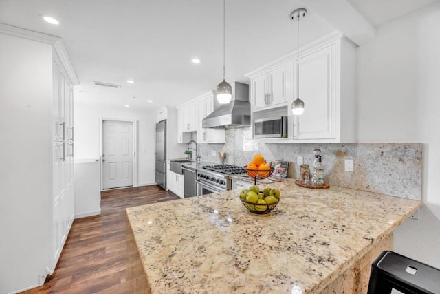 kitchen with stainless steel appliances, tasteful backsplash, kitchen peninsula, hanging light fixtures, and wall chimney range hood