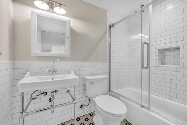 full bathroom with tile walls, tile patterned flooring, bath / shower combo with glass door, and toilet