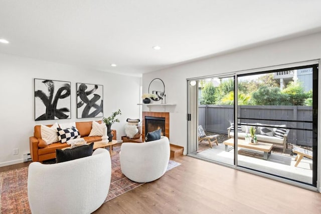 living room featuring baseboard heating, wood-type flooring, and a tiled fireplace