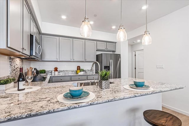 kitchen featuring kitchen peninsula, light stone counters, stainless steel appliances, and pendant lighting