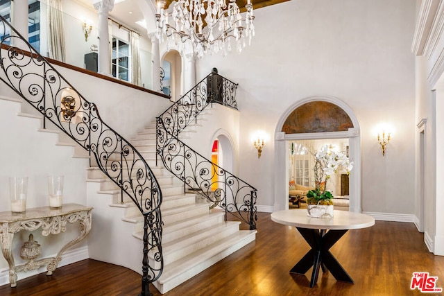 entrance foyer with decorative columns, a chandelier, wood-type flooring, and a towering ceiling