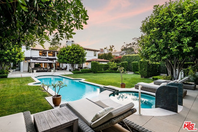 pool at dusk featuring a patio area and a lawn