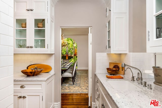 kitchen with backsplash, sink, light stone counters, and white cabinetry