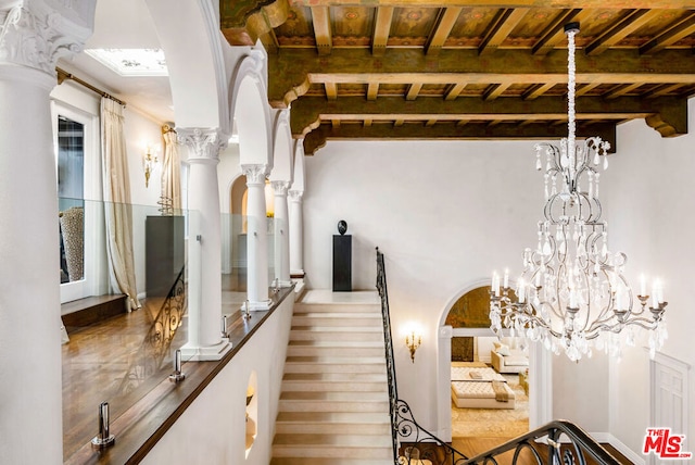 stairs featuring beam ceiling, wooden ceiling, and ornate columns