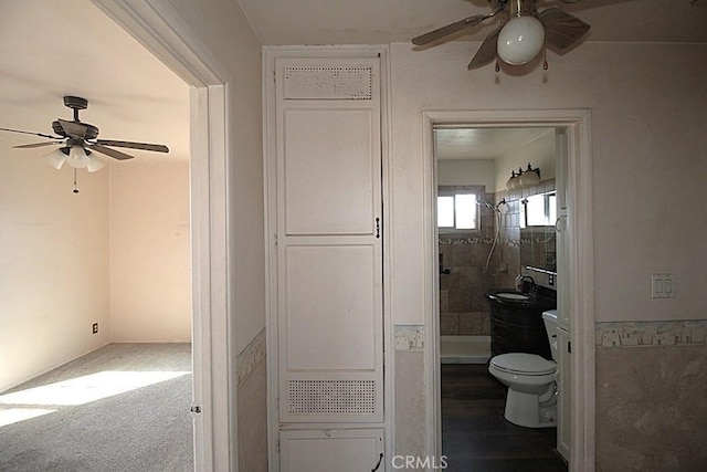 bathroom with ceiling fan, sink, toilet, and tiled shower