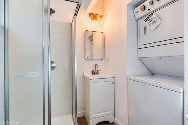 bathroom featuring stacked washer and clothes dryer, a shower with shower door, and vanity