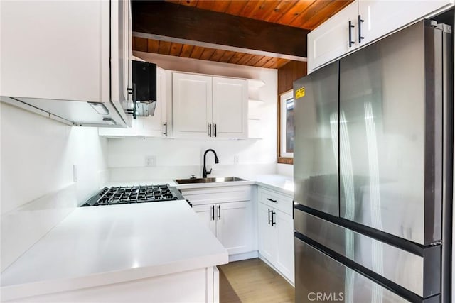 kitchen featuring white cabinetry, sink, stainless steel refrigerator, wooden ceiling, and beam ceiling