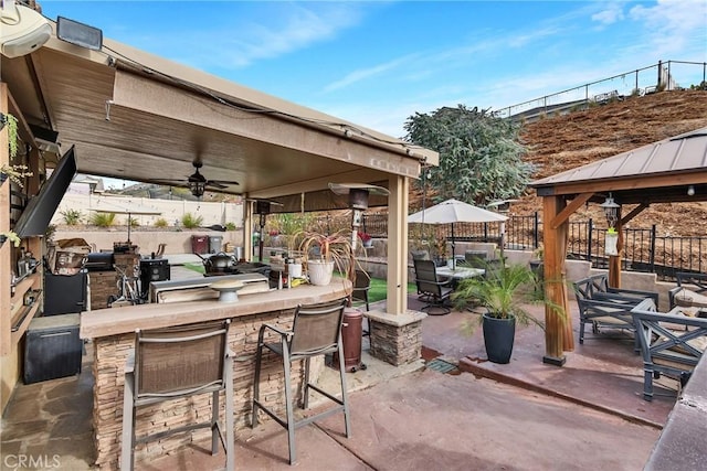 view of patio / terrace with ceiling fan, an outdoor bar, a gazebo, and an outdoor kitchen