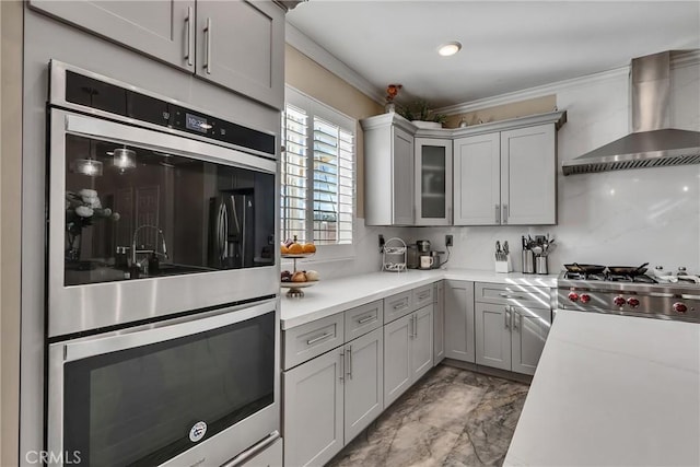 kitchen featuring wall chimney range hood, double oven, ornamental molding, and gray cabinetry