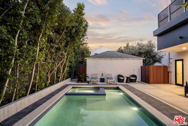 pool at dusk featuring a patio area and an in ground hot tub