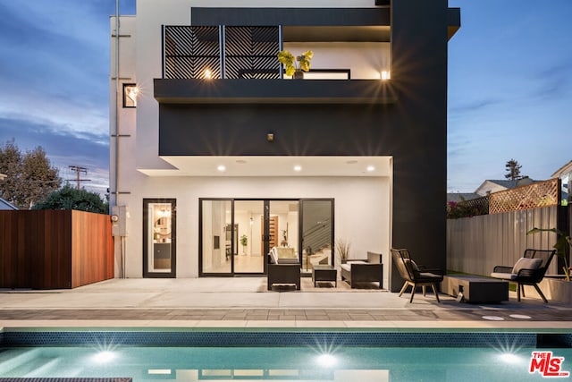 back house at dusk with a balcony, a patio area, and a fenced in pool