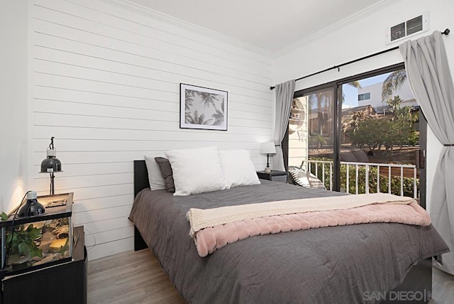 bedroom with access to exterior, wooden walls, ornamental molding, and light hardwood / wood-style floors