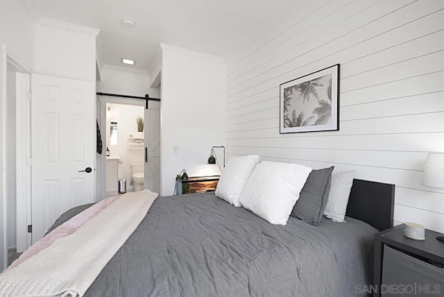 bedroom with ensuite bathroom, crown molding, a barn door, and wood walls