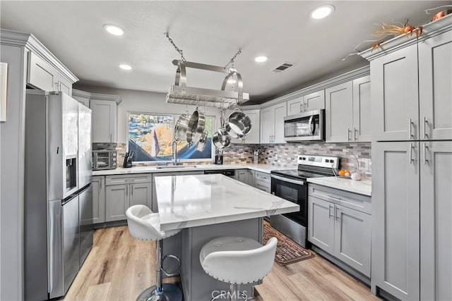 kitchen with stainless steel appliances, gray cabinetry, tasteful backsplash, and a center island